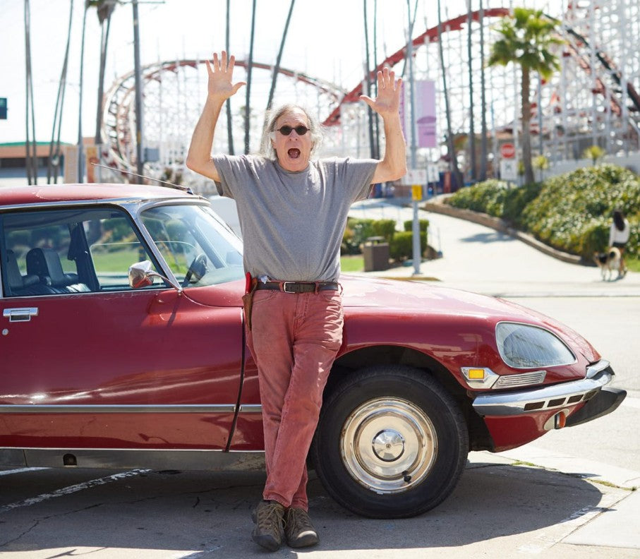 2020's photo of Randall Grahm, arms raised in the air and frightened look on his face, standing in front of his red Citroen a roller coaster in the background.