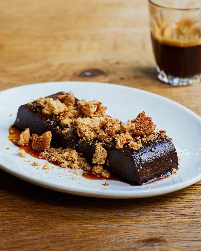 Chocolate dessert topped with crumbled amaretti on a white plate, with espresso in a glass nearby