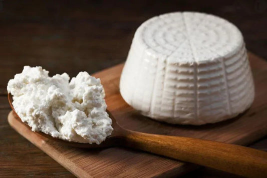 Ricotta cheese in a wooden spoon beside a round mold on a cutting board