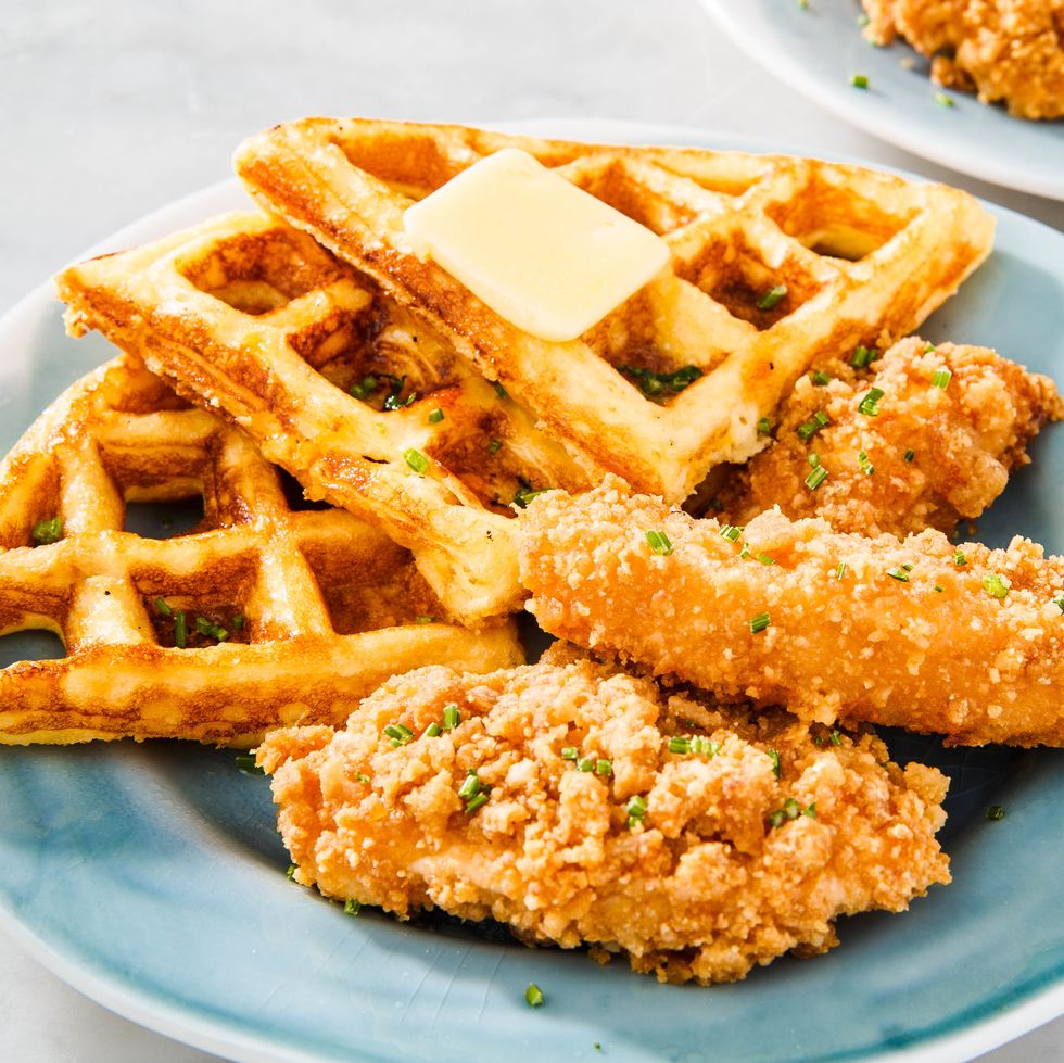 Chicken and waffles on a blue plate, topped with a pat of butter and chopped chives
