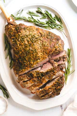 Roasted leg of lamb sliced on a white platter with fresh rosemary sprigs