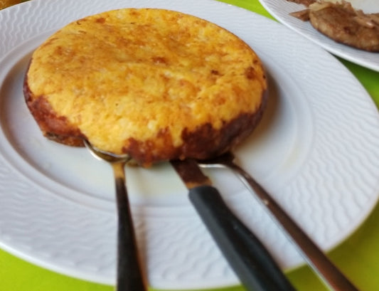 Golden round frico on a white plate with three knives underneath