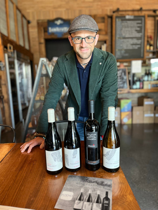 Giuseppe standing behind a table with four of his imported wines.