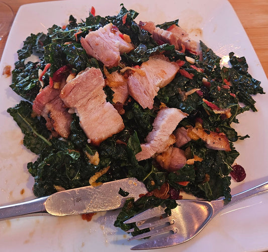 Roasted pork belly on kale salad on a white plate with serving utensils