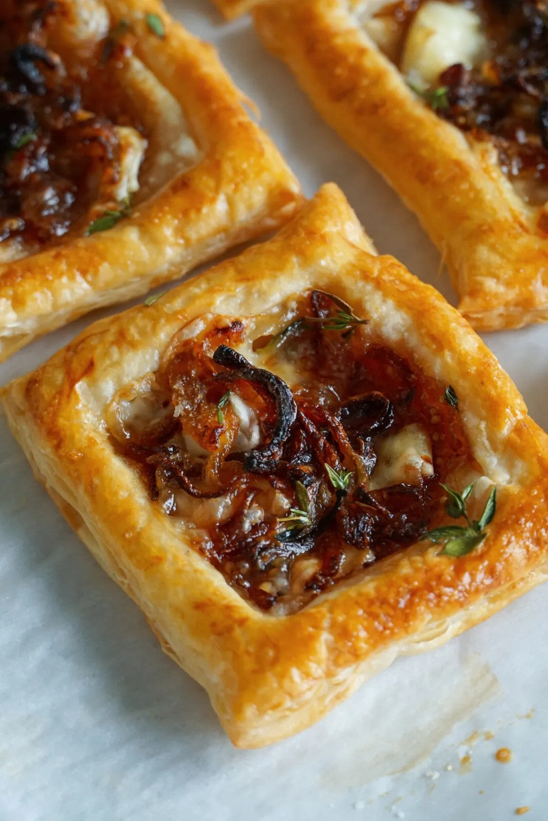 Baked brie and onion tarts with golden puff pastry and thyme garnish