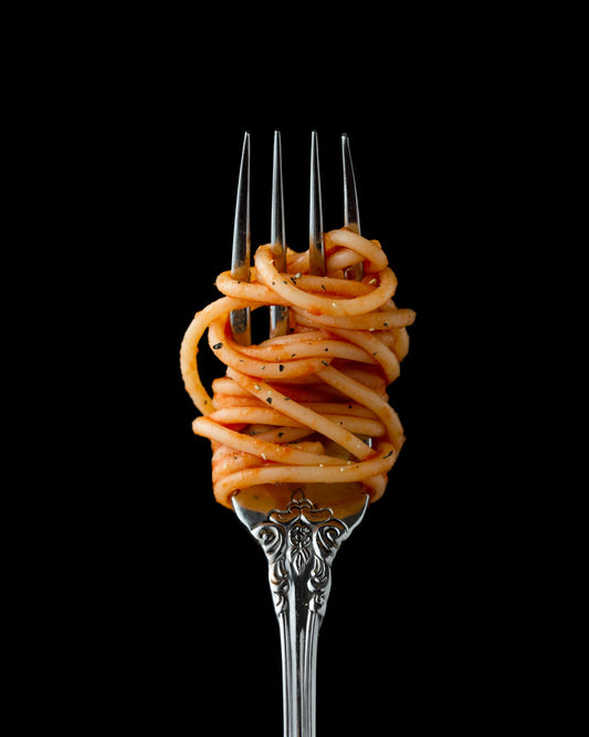 Spaghetti twirled around a silver fork against a black background