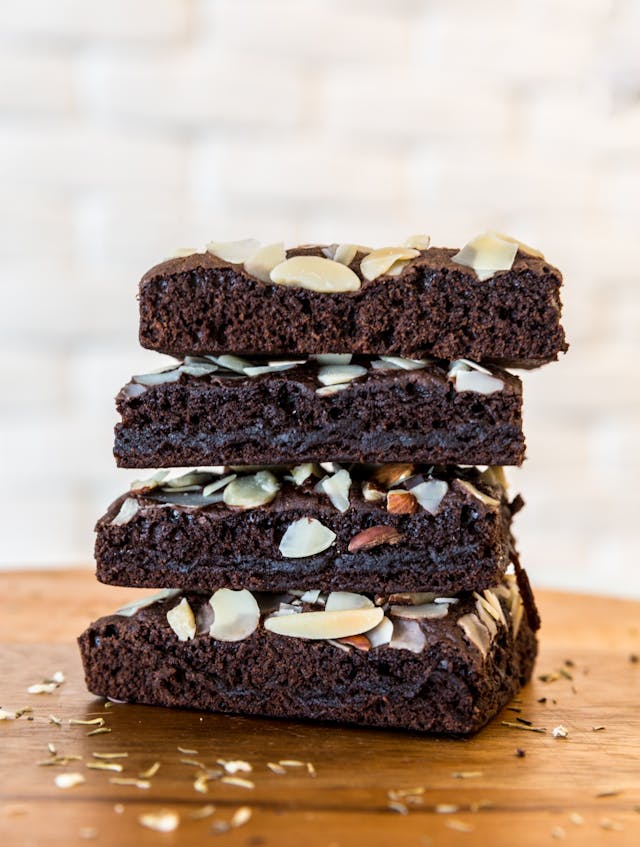Stack of chocolate brownies topped with almond slices on a wooden board