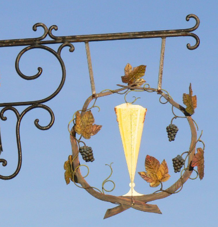 Decorative wrought iron sign with a Champagne glass and leaves against a clear blue sky