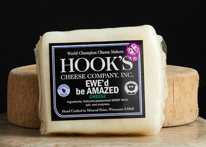 Hook's Ewe'd be Amazed cheddar. A cryo-wrapped cheese no a cutting board with black background.