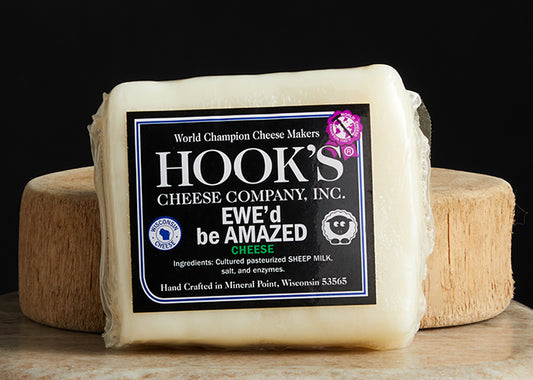 Hook's Ewe'd be Amazed cheddar. A cryo-wrapped cheese no a cutting board with black background.