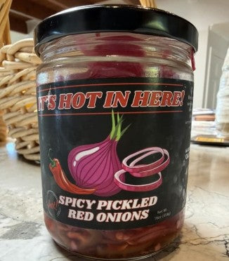 Jar of spicy pickled red onions with a black lid on a woven surface.