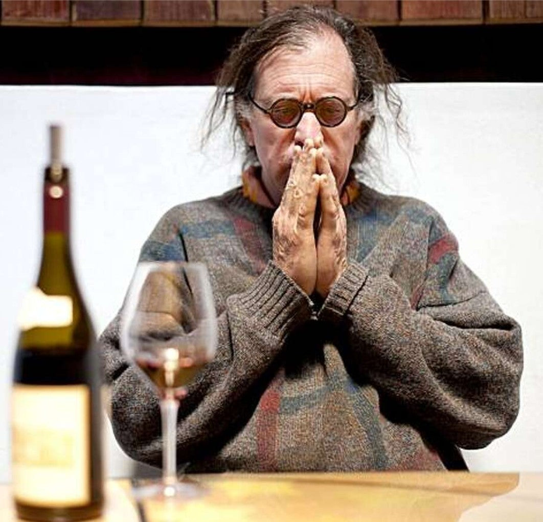 2020's photo of iconic winemaker Randall Grahm in deep contemplation as he sits with a wine bottle and glass.