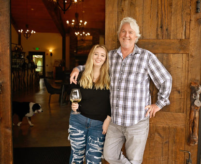 Laurent standing in front of the Serene Estate tasting room with his daughter as a dog walks through the background.